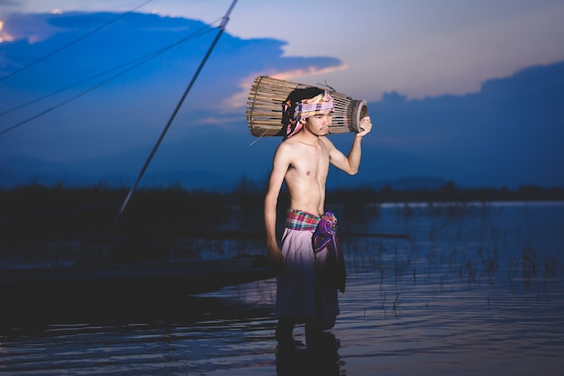 el hombre de la pesca utiliza una trampa de peces de bambú para atrapar peces en el lago al atardecer