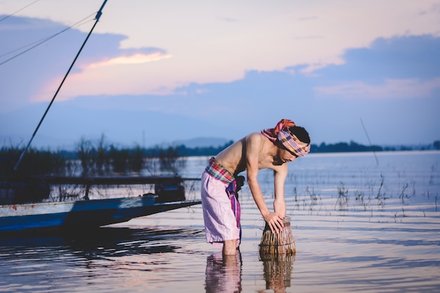 el hombre de la pesca utiliza una trampa de peces de bambú para atrapar peces en el lago al atardecer