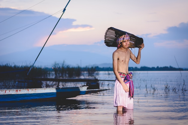 el hombre de la pesca utiliza una trampa de peces de bambú para atrapar peces en el lago al atardecer