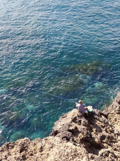 Foto un hombre está pescando en un acantilado por encima del océano