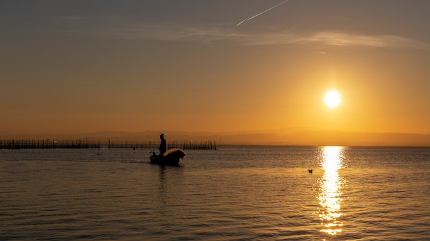 Hombre pescando en un barco al atardecer en la Albufera de Valencia.