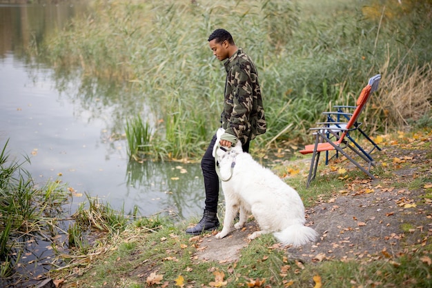 Hombre pescando cerca de un perro en la costa del río o del lago