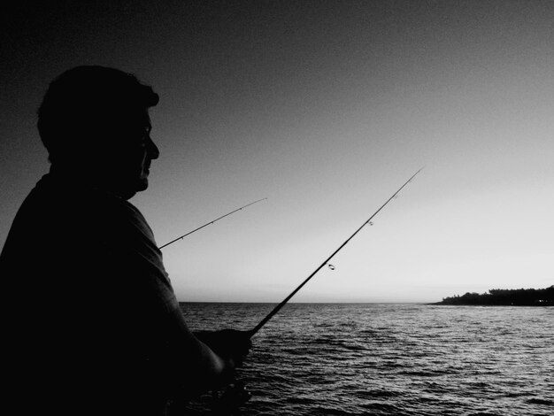 Foto hombre pescando en el mar contra un cielo despejado