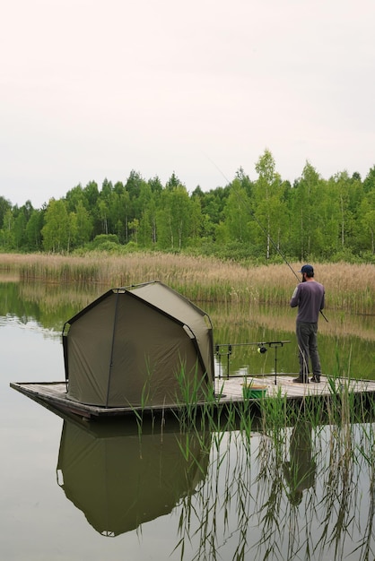 Hombre pescando con tienda de campaña en la orilla del lago Supervivencia conceptauthentic viaje vista vertical