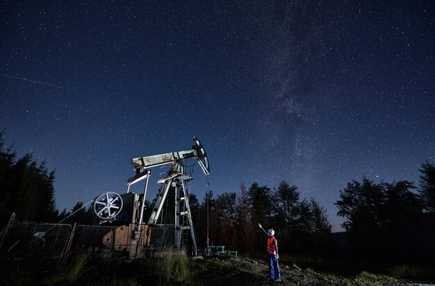 Hombre de petróleo de pie cerca de la bomba Jack bajo el cielo estrellado de la noche