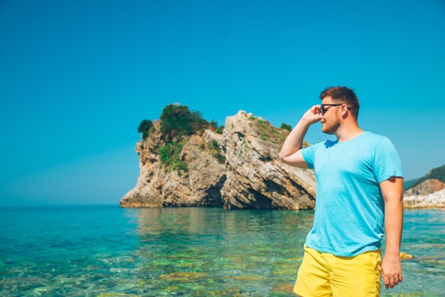 Hombre de pie con agua de mar azul claro en el fondo