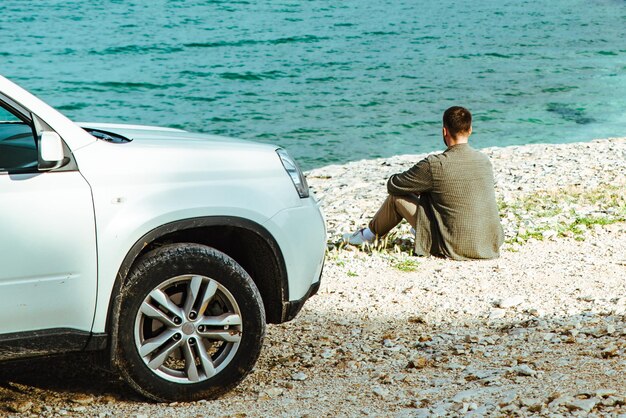 Hombre de pie cerca del coche en el concepto de viaje por carretera junto al mar