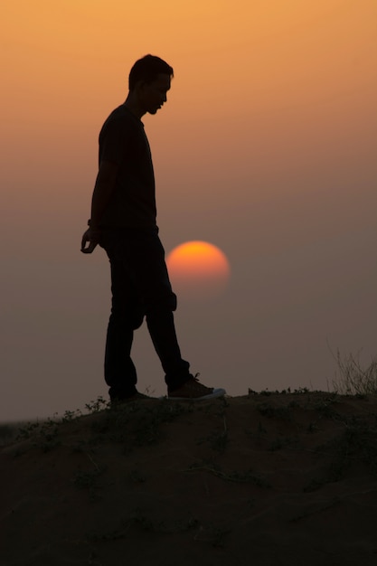 Hombre de pie en la duna de arena con puesta de sol, Jaisalmer, India