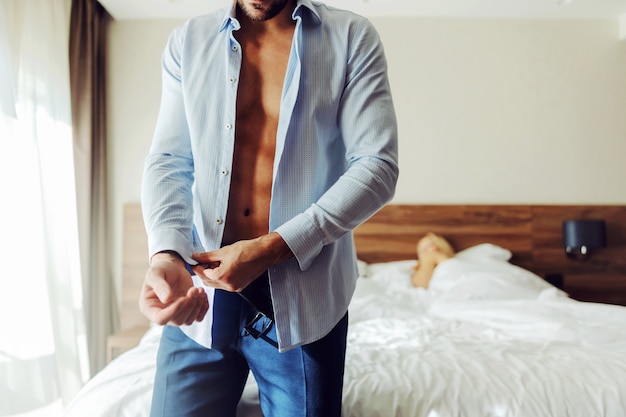 Hombre de pie junto a una cama en una habitación de hotel y abotonarse una camisa.