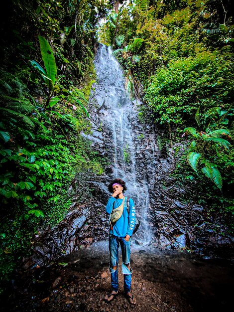 Hombre de pie junto a una cascada en el bosque