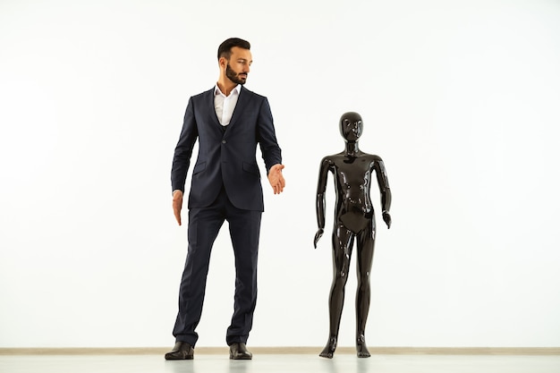 El hombre de pie con un maniquí negro sobre fondo blanco.