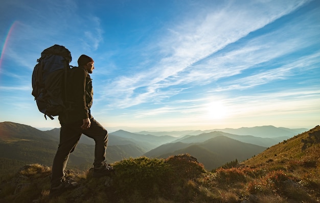 El hombre de pie con una mochila de camping en la roca con una pintoresca puesta de sol