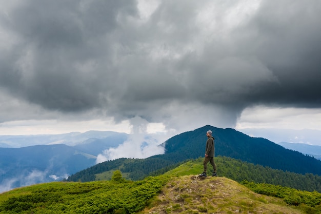 El hombre de pie en la montaña contra las nubes lluviosas.