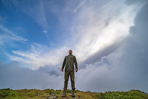 El hombre de pie en la montaña sobre un fondo de cielo nublado