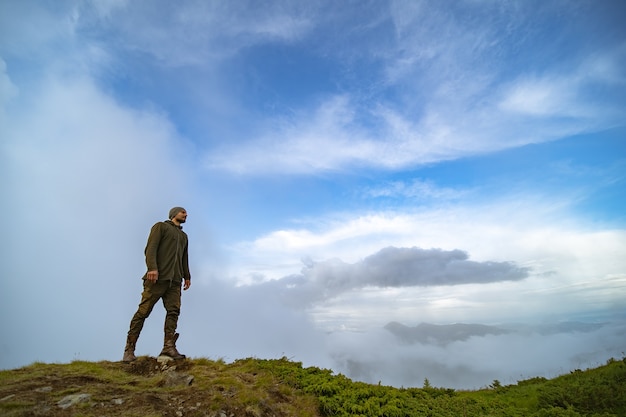 El hombre de pie en la montaña sobre el fondo de nubes blancas