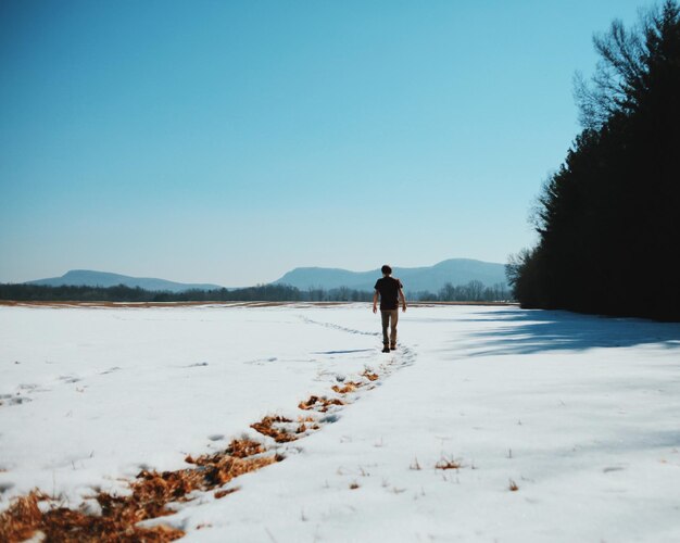 Hombre de pie en un paisaje cubierto de nieve contra un cielo despejado