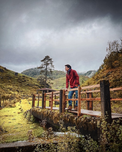 Foto hombre de pie en un puente mirando el horizonte en medio de la naturaleza y el bosque con una nube