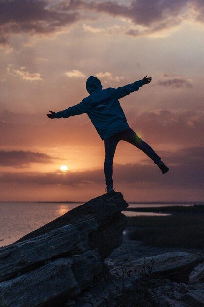 Foto hombre de pie en una roca junto al mar contra el cielo durante la puesta de sol