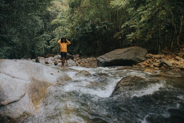 Foto hombre de pie en una roca junto al río en el bosque