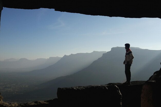 Foto hombre de pie en una roca mirando montañas idílicas