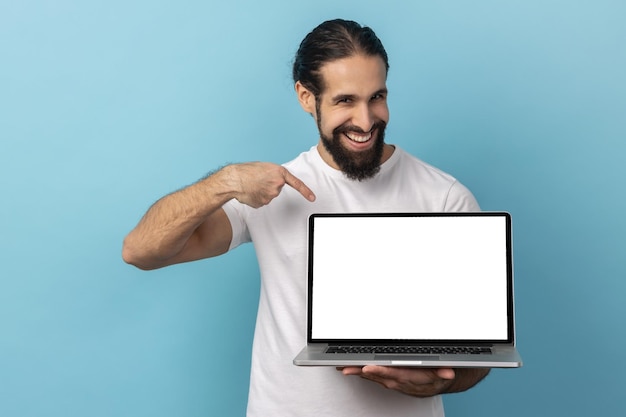 Hombre de pie sosteniendo una computadora portátil con pantalla en blanco y sonriendo a la cámara de publicidad en Internet