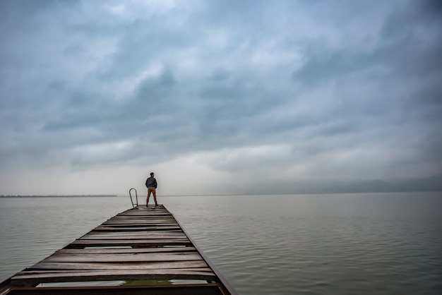 Hombre de pie en un viejo muelle de madera en clima tempestuoso