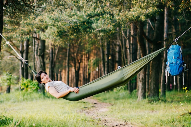 Hombre de piel roja joven peruano feliz que descansa y que se relaja en la hamaca al aire libre en la naturaleza en bosque en día soleado del verano con los pinos y la hierba verde. Viajes, vacaciones, turismo, vacaciones. Soñando en el parque.