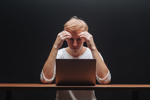 El hombre piensa en una computadora portátil con una camiseta blanca sobre un fondo negro