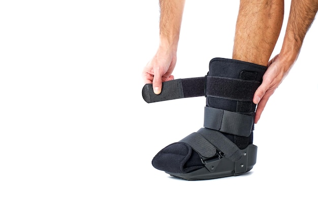 Foto hombre con la pierna en perfil poniéndose una bota ortopédica para roturas y esguinces sobre un fondo blanco