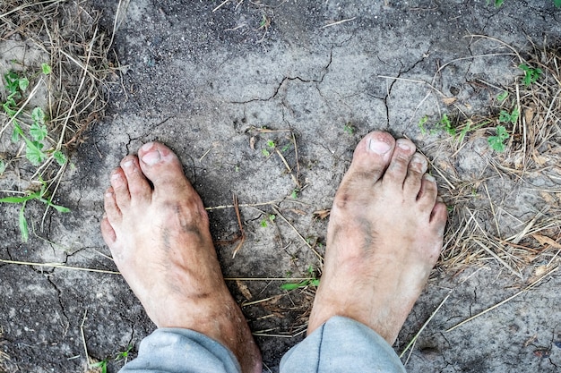 Un hombre con los pies sucios está en el suelo agrietado por el calor