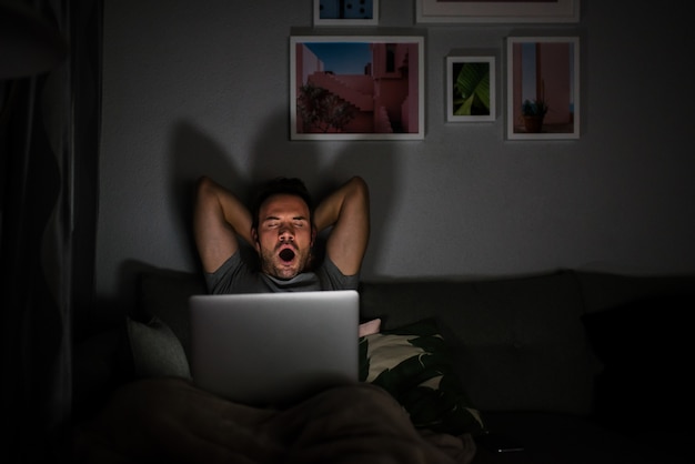 Hombre en pijama con una computadora bostezando