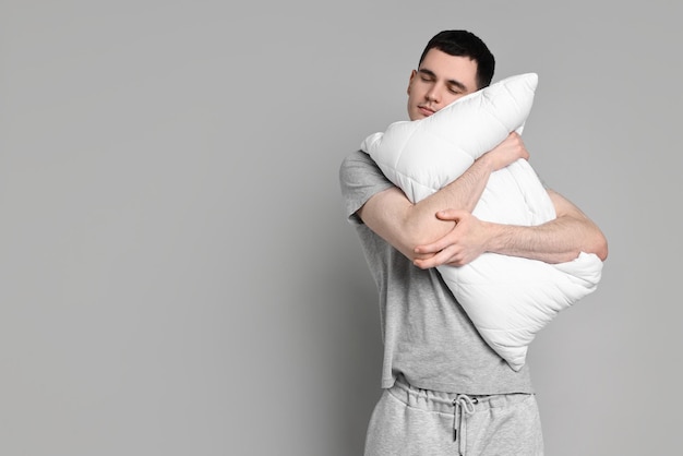 Hombre en pijama sosteniendo almohada y durmiendo en el espacio de fondo gris para el texto
