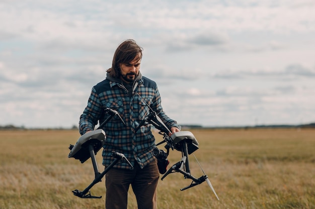 Hombre piloto sosteniendo un dron quadcopter en las manos en el campo exterior