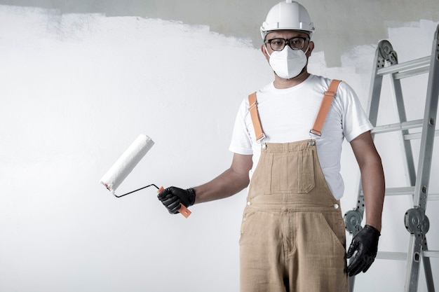 Un hombre pinta una pared blanca con un rodillo. Reparación del interior.