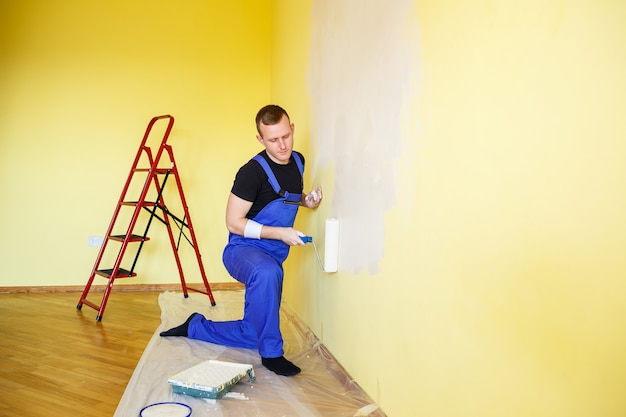 Un hombre pinta la pared de la casa con un rodillo y pintura. Reforma de estancias de la casa.