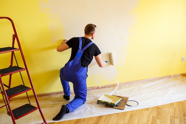 Un hombre pinta la pared de la casa con un rodillo y pintura. Reforma de estancias de la casa.