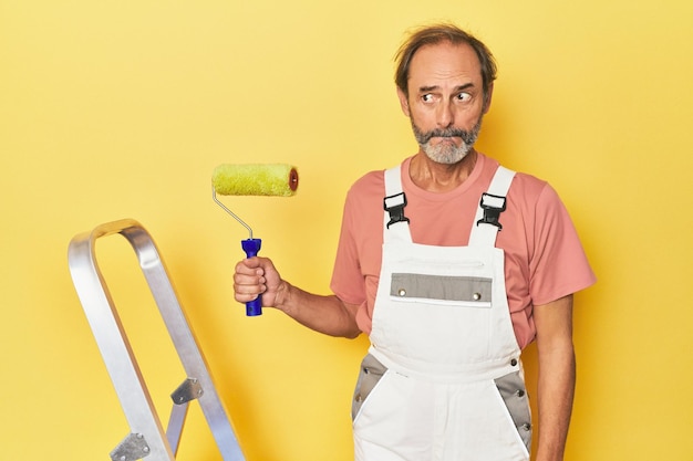 Foto el hombre pintando un fondo amarillo en el estudio confundido se siente dudoso e inseguro