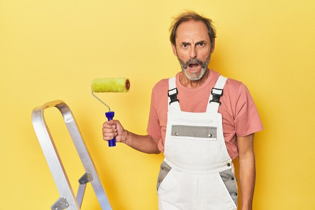 Foto hombre pintando fondo amarillo en el estudio gritando muy enojado y agresivo