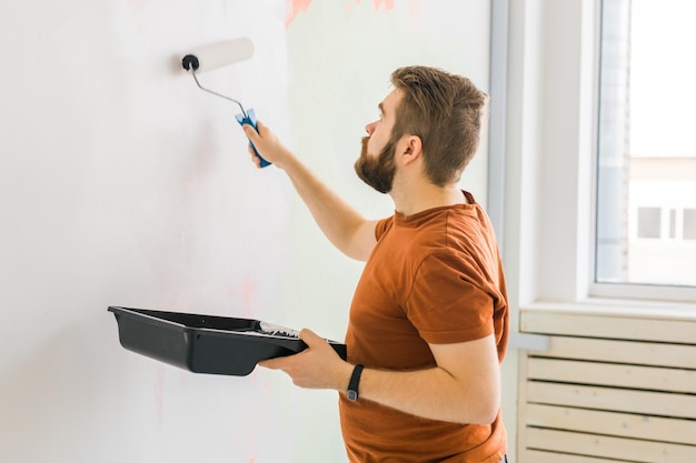 Hombre pintando la pared con el concepto de renovación y redecoración de rodillos de pintura