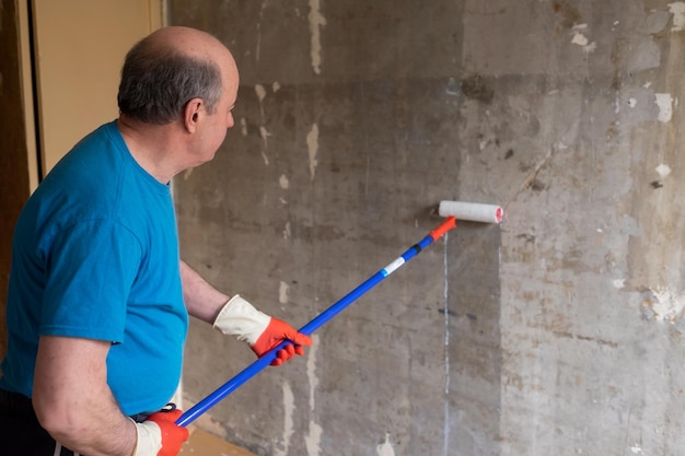 Hombre pintando paredes de cemento con cepillo de rodillos e imprimación haciendo una renovación