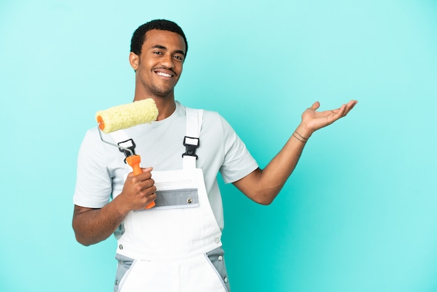 Hombre pintor afroamericano sobre fondo azul aislado extendiendo las manos hacia el lado para invitar a venir