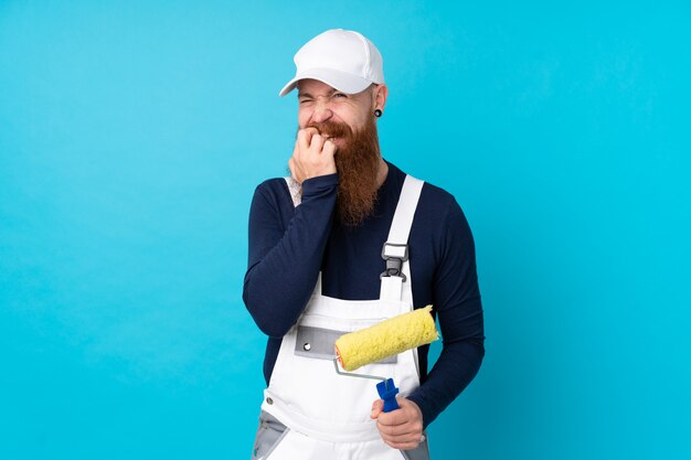 Hombre pintor con barba larga sobre pared azul aislado nervioso y asustado