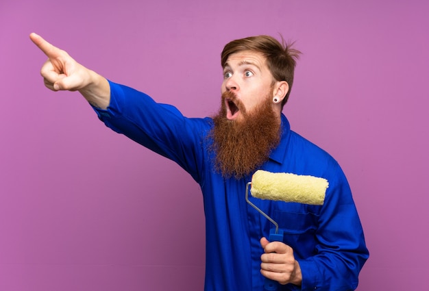 Hombre pintor con barba larga sobre púrpura aislado apuntando lejos