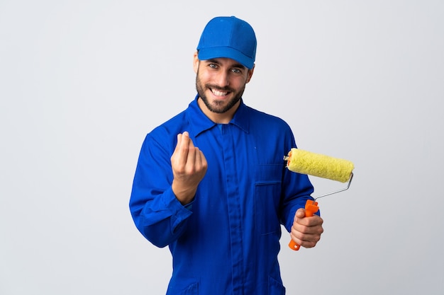 Hombre pintor sosteniendo un rodillo de pintura aislado en blanco haciendo gesto de dinero