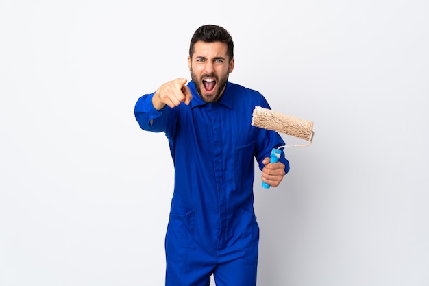 Foto hombre pintor sosteniendo un rodillo de pintura aislado sobre fondo blanco frustrado y apuntando hacia el frente