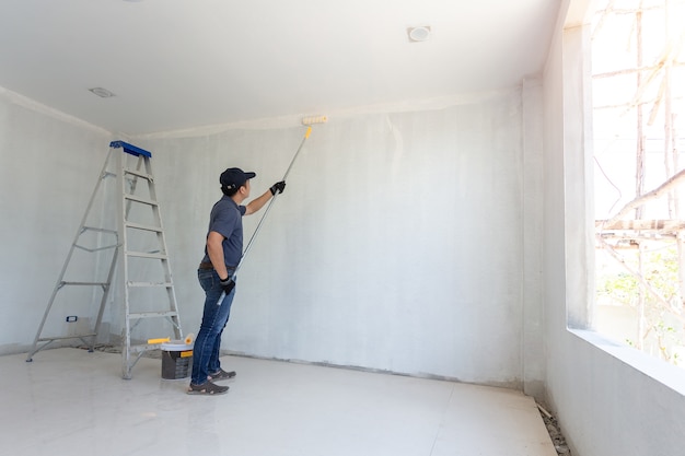 Hombre pintor en el trabajo con un rodillo de pintura en la pared