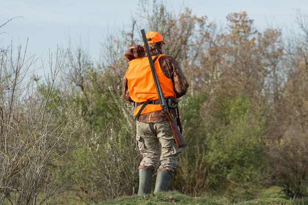 Un hombre con una pistola en las manos y un chaleco naranja en una cacería de faisanes en una zona boscosa en tiempo nublado Cazador con perros en busca de juego