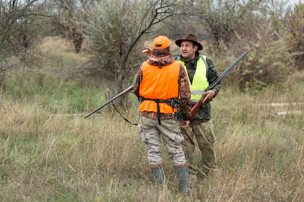 Un hombre con una pistola en las manos y un chaleco naranja en una cacería de faisanes en una zona boscosa en tiempo nublado Cazadores con perros en busca de juego