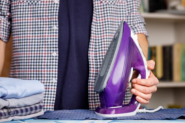 Un hombre plancha una camisa sobre una tabla de planchar con una plancha. Tareas domésticas diarias.