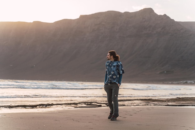 Hombre en la playa con el acantilado de fondo viendo la puesta de sol